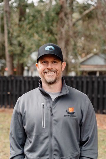 A man wearing a hat and jacket standing in front of a fence.